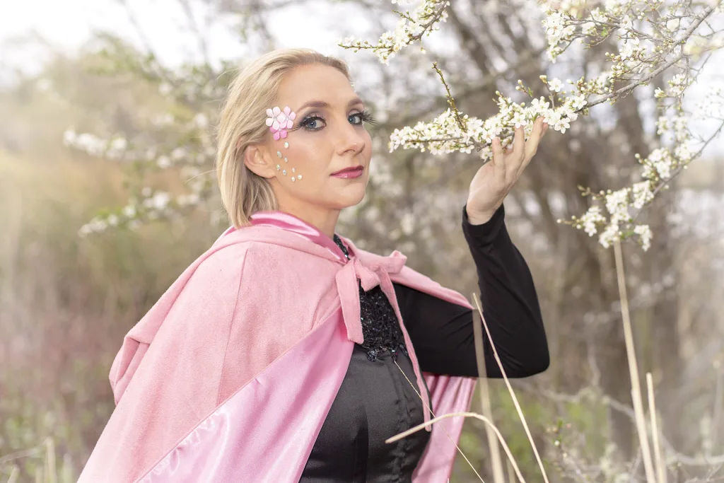 Portrait of a woman wearing a pink cloak holding a flower.